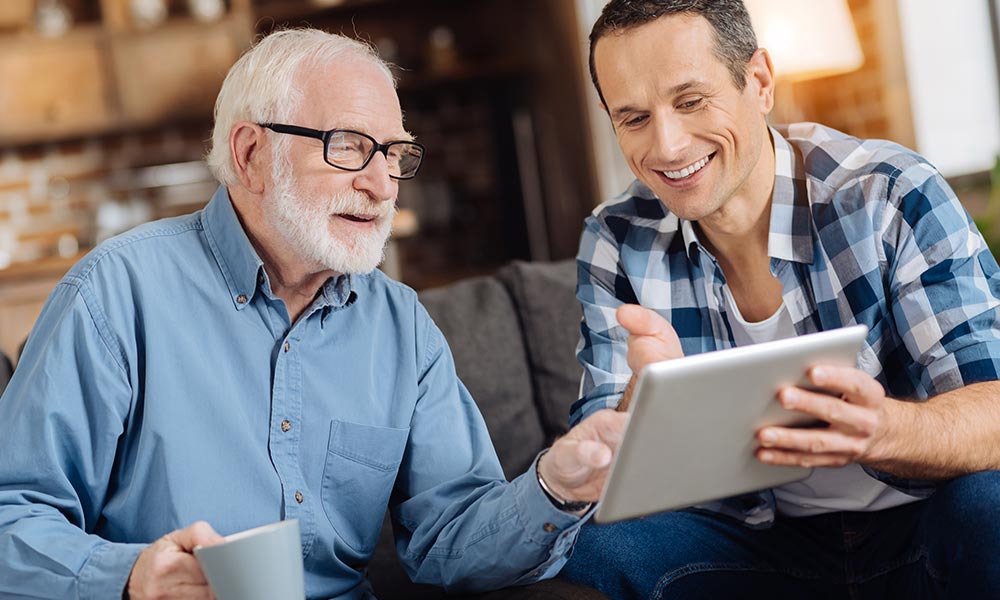 Elderly gentleman being assisted with technology by his son