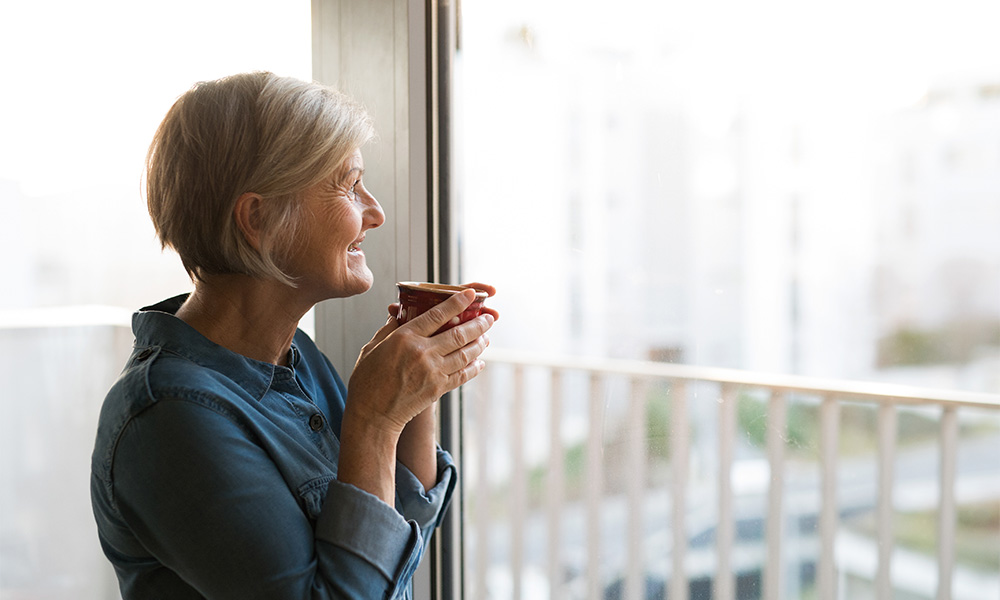 retired woman looking out the window of her apartment